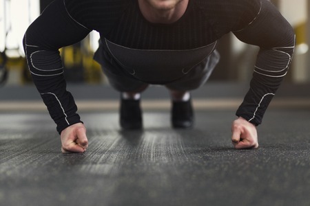 Young man workout in fitness club. Unrecognizable guy making plank or push ups exercise on fists,...