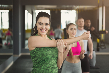 Young smiling woman stretching hands in fitness club. Cheerful female fitness coach warming up, preparing for group training, copy spaceの写真素材