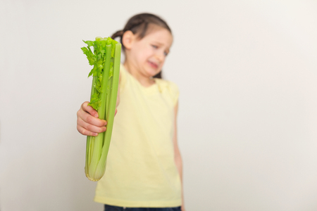Disgusted little girl standing with celery over white background. Healthy food for children concept, disgust, dislike, selective focus, copy spaceの写真素材