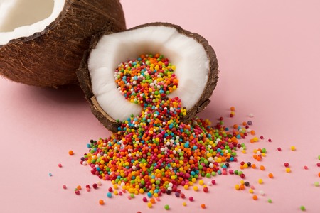 Ripe coconut halves with colorful candy sprinkles inside on pink studio backdrop. Creative background, Easter greeting card design, copy spaceの写真素材