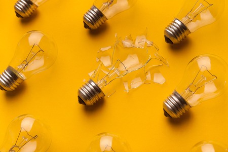 One broken light bulb among whole ones on yellow background, side view, closeup. Creativity and fragility conceptの写真素材