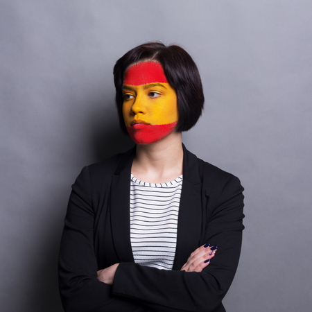 Face of young desparate woman painted with flag of Spain. Football or soccer team fan, sport event, faceart and patriotism concept. Studio shot at gray background, copy spaceの写真素材