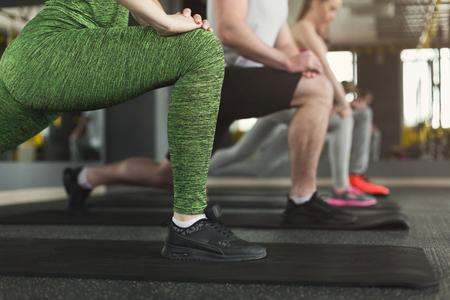 Unrecognizable fitness group warmup stretching training at indoors. Legs of athletes making aerobics exercise at gym, copy spaceの写真素材