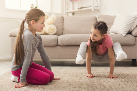 Little girls or sisters training yoga together indoors, at home. Family, sport, yoga, health conceptの写真素材