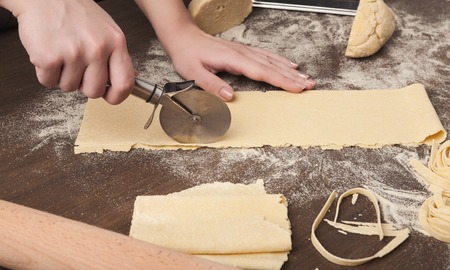Cutting raw dough. Chef using wheel cutter in preparation of italian pasta on kitchen table, copy spaceの写真素材