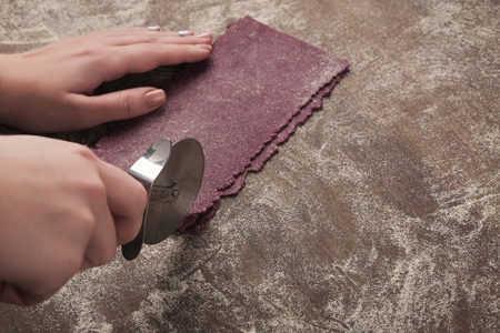 Cutting purple raw dough. Chef using wheel cutter in preparation of unusual black currant italian...