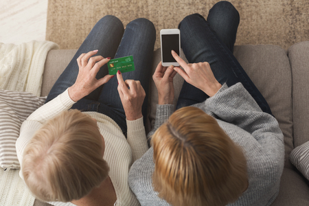 Adult woman holding credit cart and daughter pointing on smartphone with blank screen, copy space. Generation, relationship, modern technology, shopping online concept, top viewの写真素材