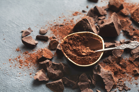 Dark chocolate pieces crushed on dark background and cocoa powder closeup, copy space. Sweet wallpaper, confectionery shop advertising and cooking ingredients conceptの写真素材