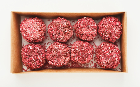 Raw vegan candies in red coconut flakes in craft box isolated on white background, top view. Healthy...