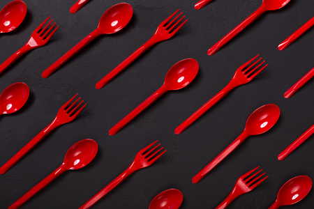 Many red plasic forks and spoons on black background, top view. Disposable table wear concept