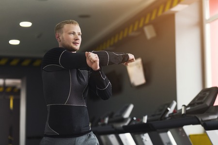 Young handsome man stretching hands in fitness club. Cardio workout, guy warming up, preparing for...