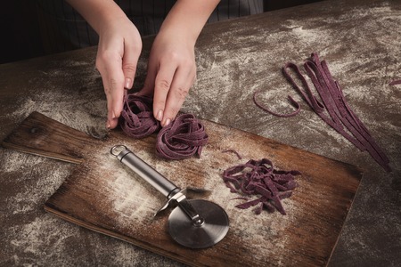 Woman chef making beetroot tagliatelle nest on kitchen table. Preparing unusual purple homemade Italian pasta, top view, copy spaceの写真素材
