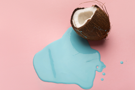 Blue paint flowing from coconut half on pink table. Creative background with copy space, bold design for poster or clothing printの写真素材