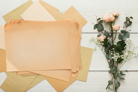 Wedding invitations and craft envelopes on white wooden background. Top view on paper cards, rings and pink roses bouquet, copy space. Memmorable date organization conceptの写真素材
