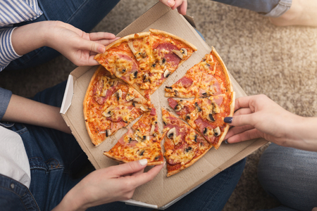 Closeup of girls hands taking pizza slices. Friendship, slumber party and fast food conceptの写真素材