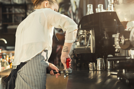 Young tattooed barista making coffee in professional coffee machine. Woman preparing beverage. Small business and professional coffee brewing conceptの写真素材