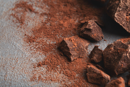 Dark chocolate pieces crushed on dark background and cocoa powder closeup, copy space. Sweet wallpaper, confectionery shop advertising and cooking ingredients conceptの写真素材