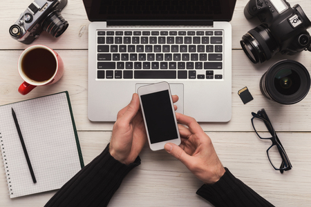 Photographer using blank smartphone on workplace with photo equipment, networking, technology and communication concept, top view, copy spaceの写真素材