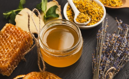 Honey assortment, closeup. Glass jar, honeycombs, pollen bowl, nuts, ginger, mint and dry oranges....