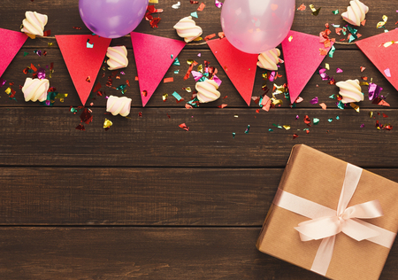 Border of pink and violet paper flags garland, marshmallows, confetti and and craft gift box on rustic wood. Birthday party decoration background, top view, copy space. Mockup for greeting cardの写真素材