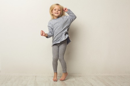 Beautiful casual little girl posing at white studio background. Full-length portrait of cute happy jumping kid, copy spaceの写真素材