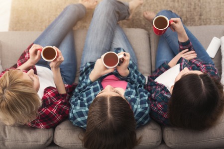 Three women drinking coffee and watching movie at home, female friends having rest after hard week, top view. Friendship and slumber party conceptの写真素材