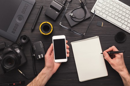 Photographer taking notes while using smartphone. Top view on creative designer workplace with photo equipment and mobile phone, timetable planning and self-education concept, copy spaceの写真素材