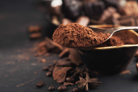 Chocolate background. Bowl and vintage spoon with cocoa powder, variety of candies and anise star on...