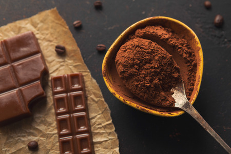 Chocolate background. Bowl and vintage spoon with cocoa powder, variety of candies and spices on...