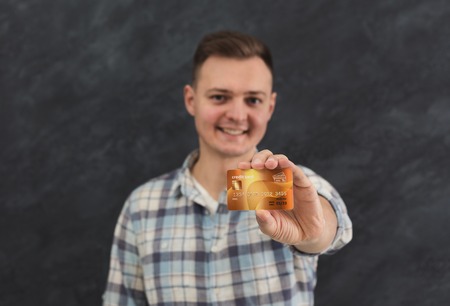 Happy man holding credit card. Young smiling bank client, sale, discount card and shopping concept, gray studio background, copy spaceの写真素材