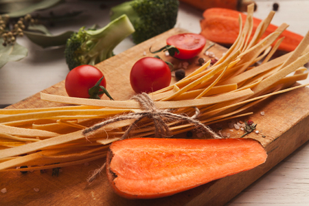 Raw handmade orange tagliatelle with carrot juice, tomatoes, broccoli and spices on white wooden table. Cooking pasta background, copy spaceの写真素材