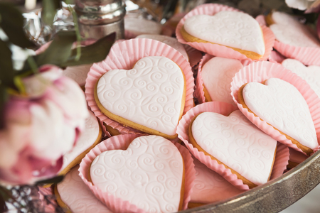 Closeup of heart shaped cookies with pink textured icing on silver tray. Baked snaks for party dessert stand. Candy bar and catering concept for birthday, wedding and other holiday celebrationの写真素材