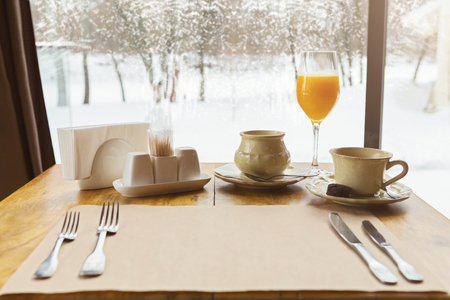 Table setting in restaurant interior against window with snowy winter scenery. Waiting for breakfast with coffee cup and orange juiceの写真素材