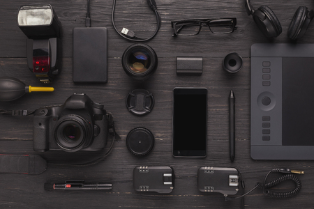 Top view on workplace of photographer or creative designer. Desk with new black photographic equipment on dark wooden table, copy spaceの写真素材