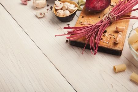 Raw handmade red tagliatelle with beetroot juice, white cannelloni, mushrooms and spices on white wooden table. Cooking pasta background, copy spaceの写真素材