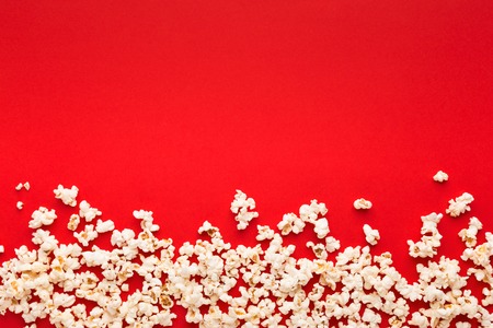 Border of popcorn scattered over red background with copy space, top view. Minimalistic design for movie poster, entertainment conceptの写真素材