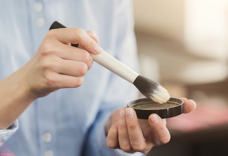 Womans hands holding cosmetic brush and powder in beauty salon, ready to do make up. Cosmetics, care, beauty conceptの写真素材