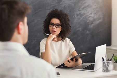 Concentrated couple of young colleagues working in modern office. Serious black woman hr interviewing male candidate, copy spaceの写真素材