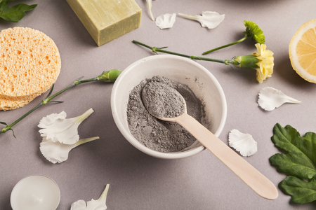 Preparing cosmetic black mud mask on gray background with various skincare products. Dry facial clay powder in bowl. Natural cosmetics for home or salon spa treatmentの写真素材