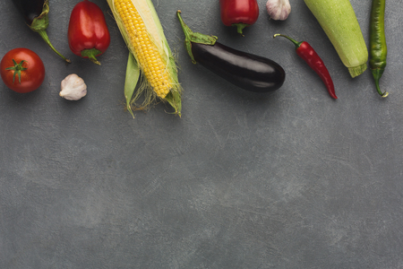 Border of fresh vegetables on grey background. Red bell pepper, cherry tomatoes, garlic, green and red chilli, eggplant, zucchini and corn on rustic table with copy space, top viewの写真素材