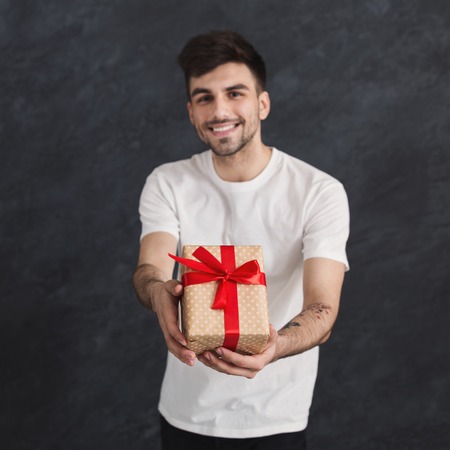 Happy man holding gift with red ribbon bow in his hands on black studio background. Christmas or Valentines Day, holiday concept, copy spaceの写真素材