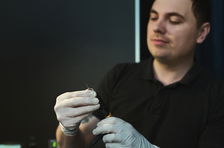 Tattooist preparing tools for procedure of drawing. Man artist changing needle on tattoo machine, safe body modification, health care and hygiene concept, copy spaceの写真素材