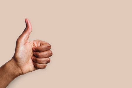 African-american hand making thumb up gesture on beige background. Close-up of positive sign, like,...