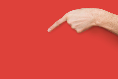 Male hand pointing on virtual object with index finger, gesturing downward on red background, close-up, copy spaceの写真素材