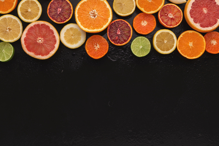 Border of assorted citruses on black background, copy space. Top view on oranges, lemons, tangerines and other exotic fruits, flat layの写真素材