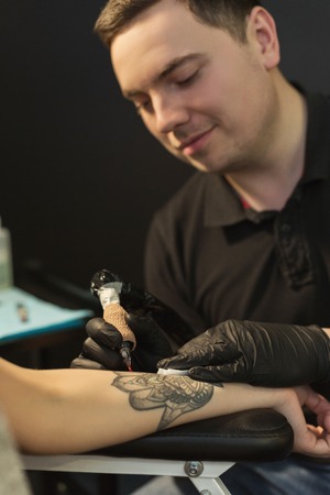 Professional tattoo artist making beautiful tattoo on young woman hand. Man tattooist drawing...