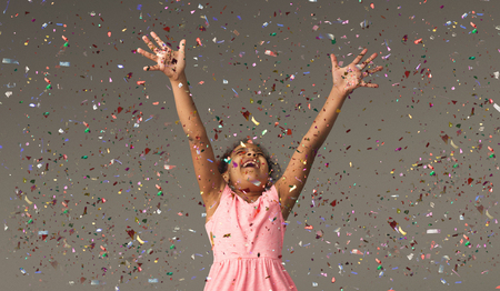 Happy african-american little girl at gray studio background, copy space. Portrait of beautiful child having fun with shiny confettiの写真素材