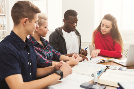 Multiethnic university students studying together. Young people working with tests and gadgets at wooden table. Education and technology concept, copy spaceの写真素材