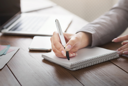 Closeup of businesswoman hand taking notes at office table with laptopの写真素材