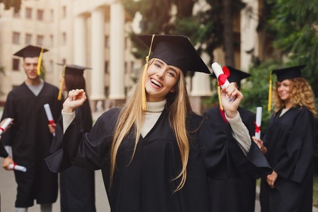 Young smiling woman on her graduation day in university, standing with multiethnic group of students. Education, qualification and gown concept.の写真素材